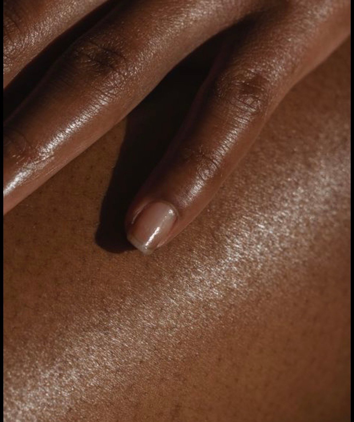 Close-up of a person's hand with manicured nails on glowing bronze skin
