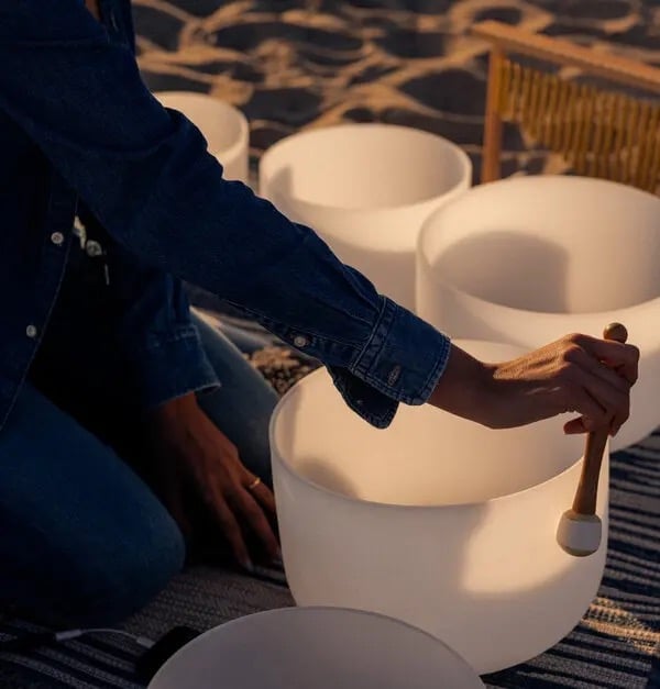 Person in denim shirt playing white cylindrical drums with wooden mallets indoors
