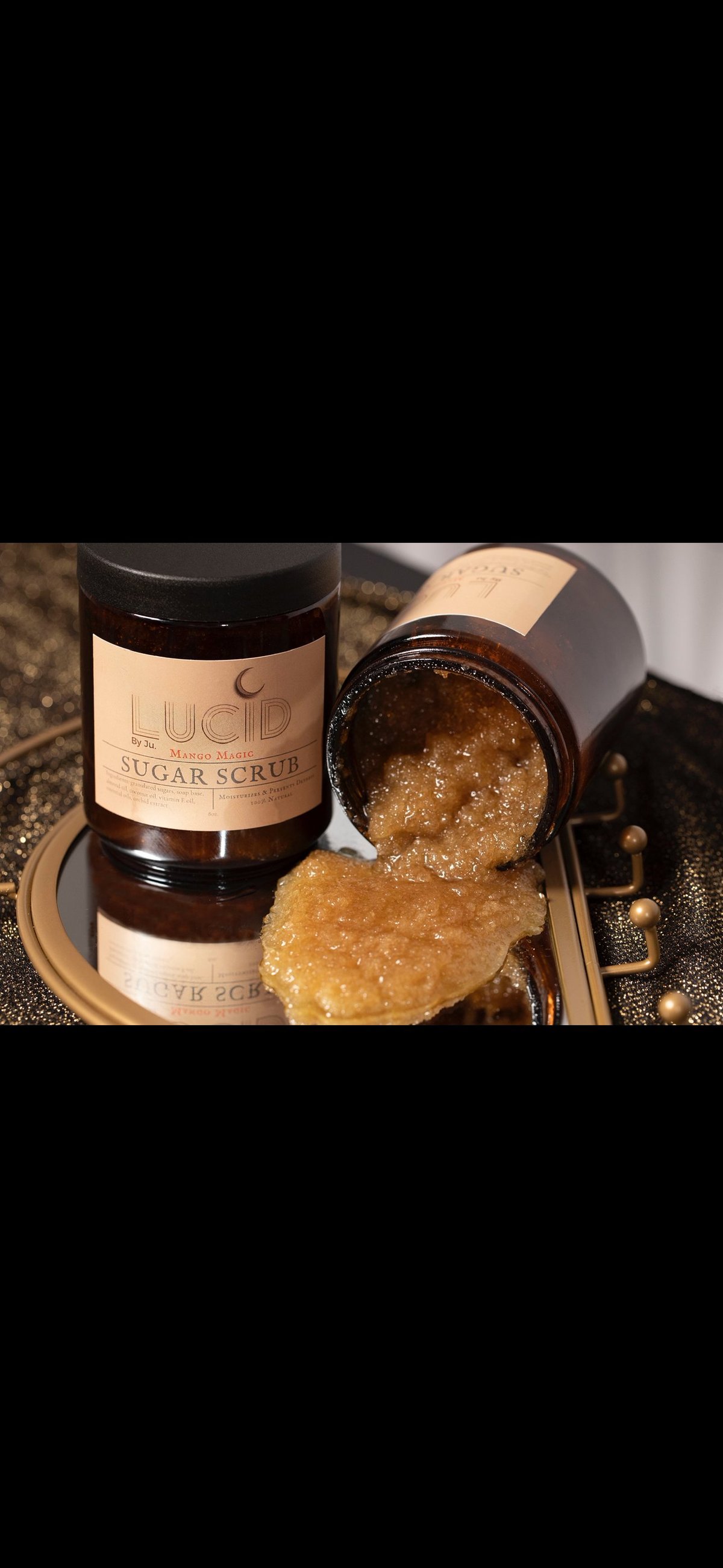 Lucid brand sugar scrub in dark glass jars with golden amber exfoliating scrub spilling out on a decorative tray