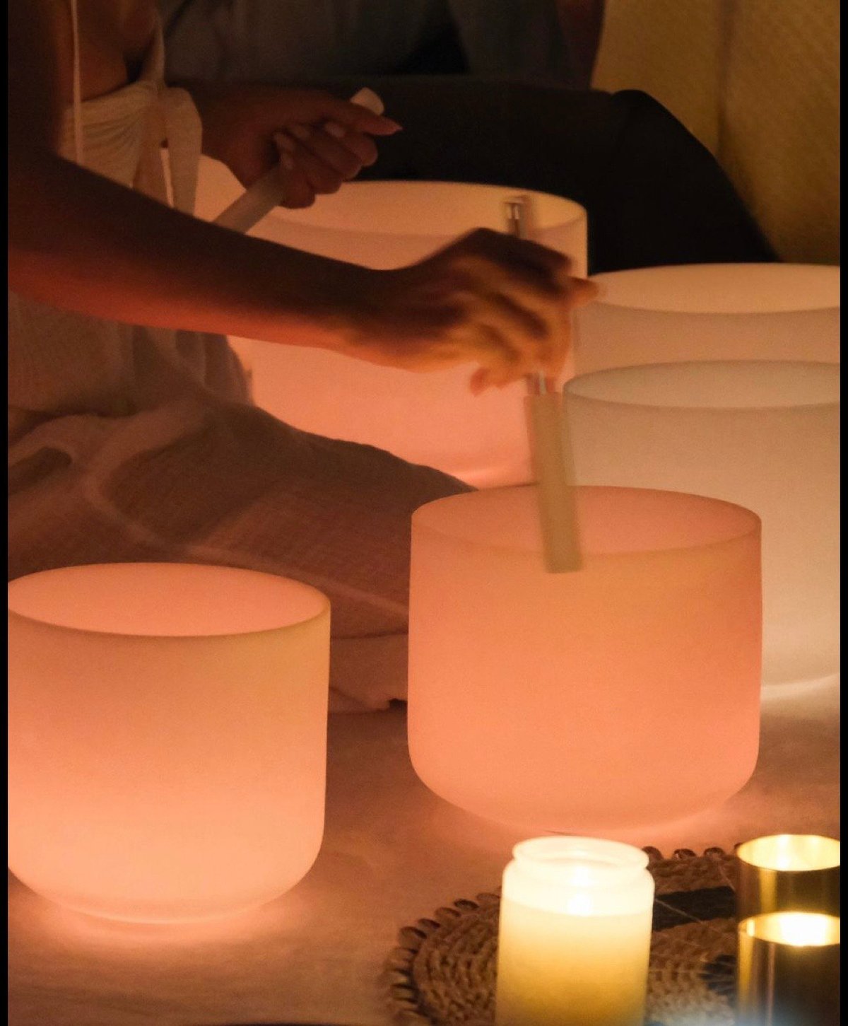 Persons hands pouring water into glowing cylindrical candles surrounded by lit candles on a table